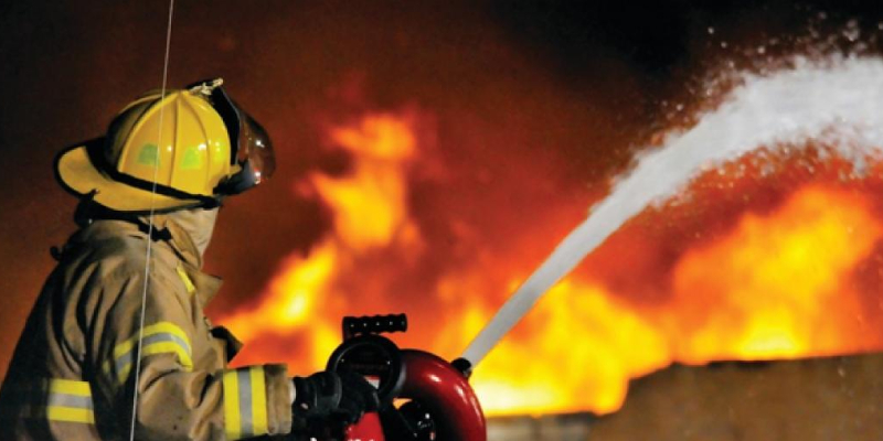 A fireman is using a fire extinguisher and putting out fire at a building in a distance.